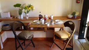 A dining area with a wooden table set for two, chairs, a coffee maker, and a vase with flowers. - The Garden Flat: a country apartment close to the beach and daywalks. (Collingwood)