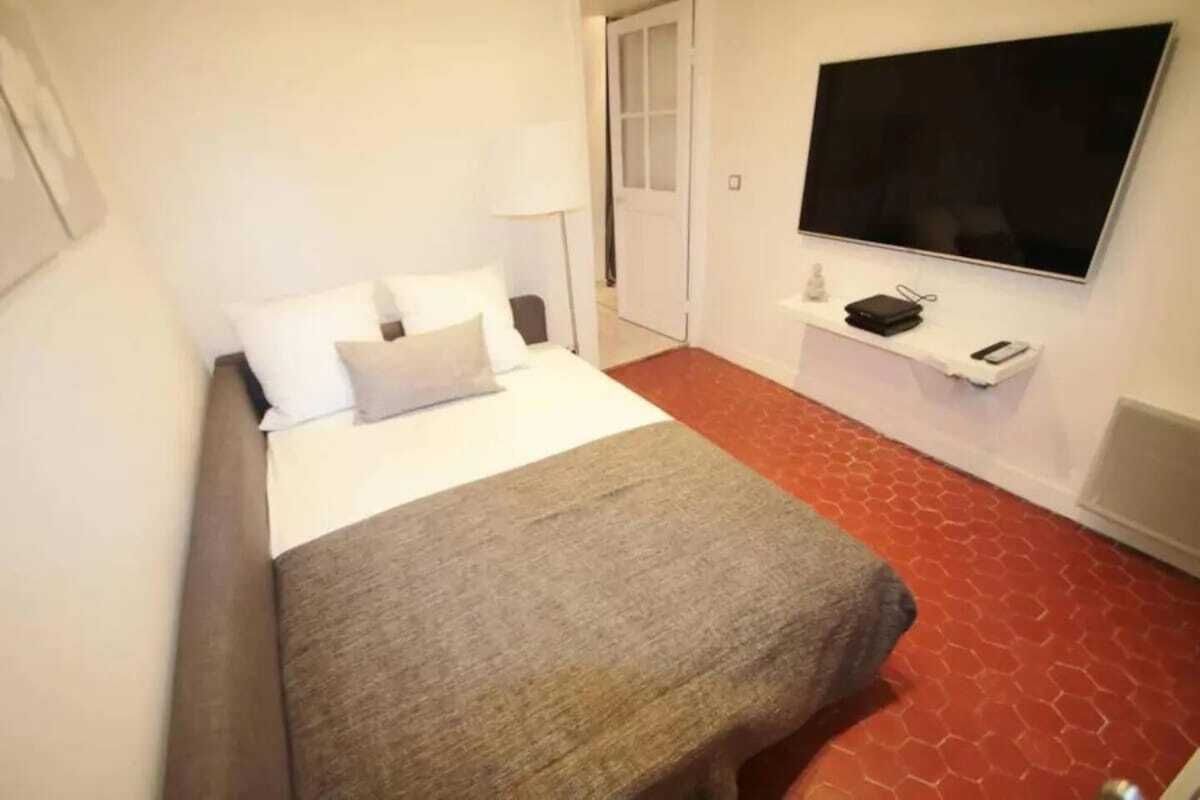 Une chambre d’hôtel avec un lit, un téléviseur fixé au mur, une petite table avec une lampe et un sol à motifs rouges.