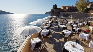 Un espace de restauration en plein air, avec des tables et des parasols, offrant une vue sur la mer, ainsi qu’une terrasse en bois et une vue sur la côte.