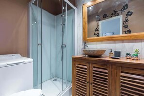 Une salle de bain dotée d’une douche à parois de verre, d’un meuble-lavabo en bois avec un vasque et d’un miroir orné d’un cadre floral.