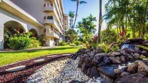 Un hotel con un jardín paisajístico que incluye una fuente de agua, palmeras y un césped bien cuidado.