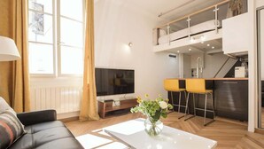 Una sala de estar moderna con un sofá, una mesa de centro con un jarrón, un televisor y una zona de cocina con una barra.