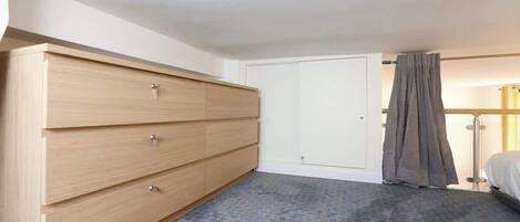 Ett hotellrum med en stor byrå i trä, en stängd dörr och en säng med en grå gardin.