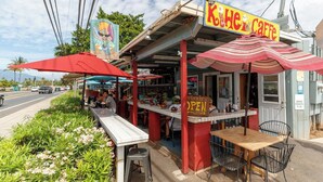 Een café met terras, een rood luifel en een bordje met de tekst 'Koh He Cafe'.