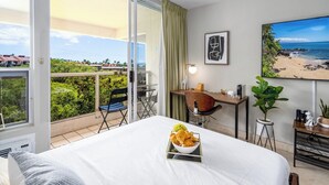 Hotelkamer met een bed, een bureau, een stoel, een eettafel, een bloempot en een groot raam met uitzicht op het strand.