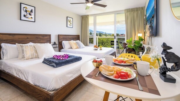 Een hotelkamer met twee bedden, een balkon, een eettafel met ontbijt en een plafondventilator.