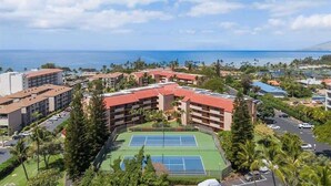 Un complexe hôtelier comprenant plusieurs bâtiments, un court de tennis et offrant une vue sur l’océan.