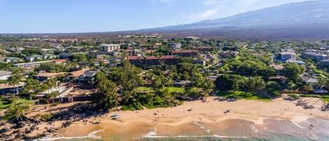An aerial view of a coastal town with a beach, buildings, and a mountain in the background.