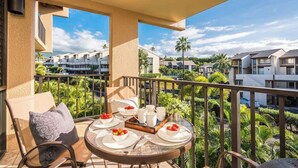 A balcony with a table set for breakfast, overlooking a residential area with palm trees and modern houses. - Luxury Maui Condo | Ocean Views + Resort Perks (Wailea-Makena)