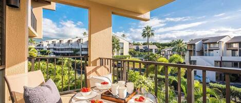 A balcony with a table set for breakfast, overlooking a residential area with palm trees and modern houses.
