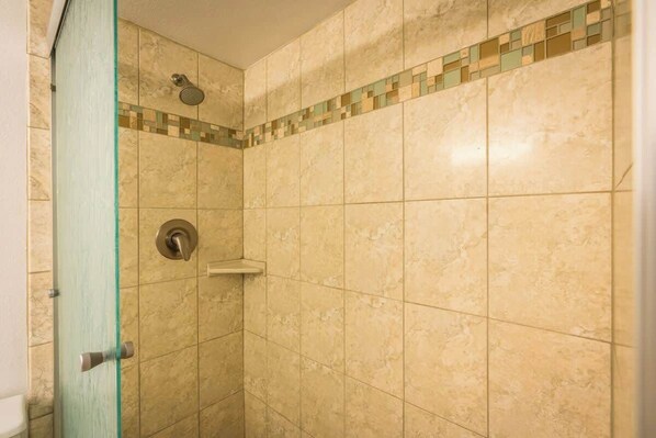 A shower with beige tiles and a green glass door.