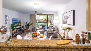 Una sala de estar moderna con comedor, un ventanal grande y una encimera de cocina con fruta y aperitivos.