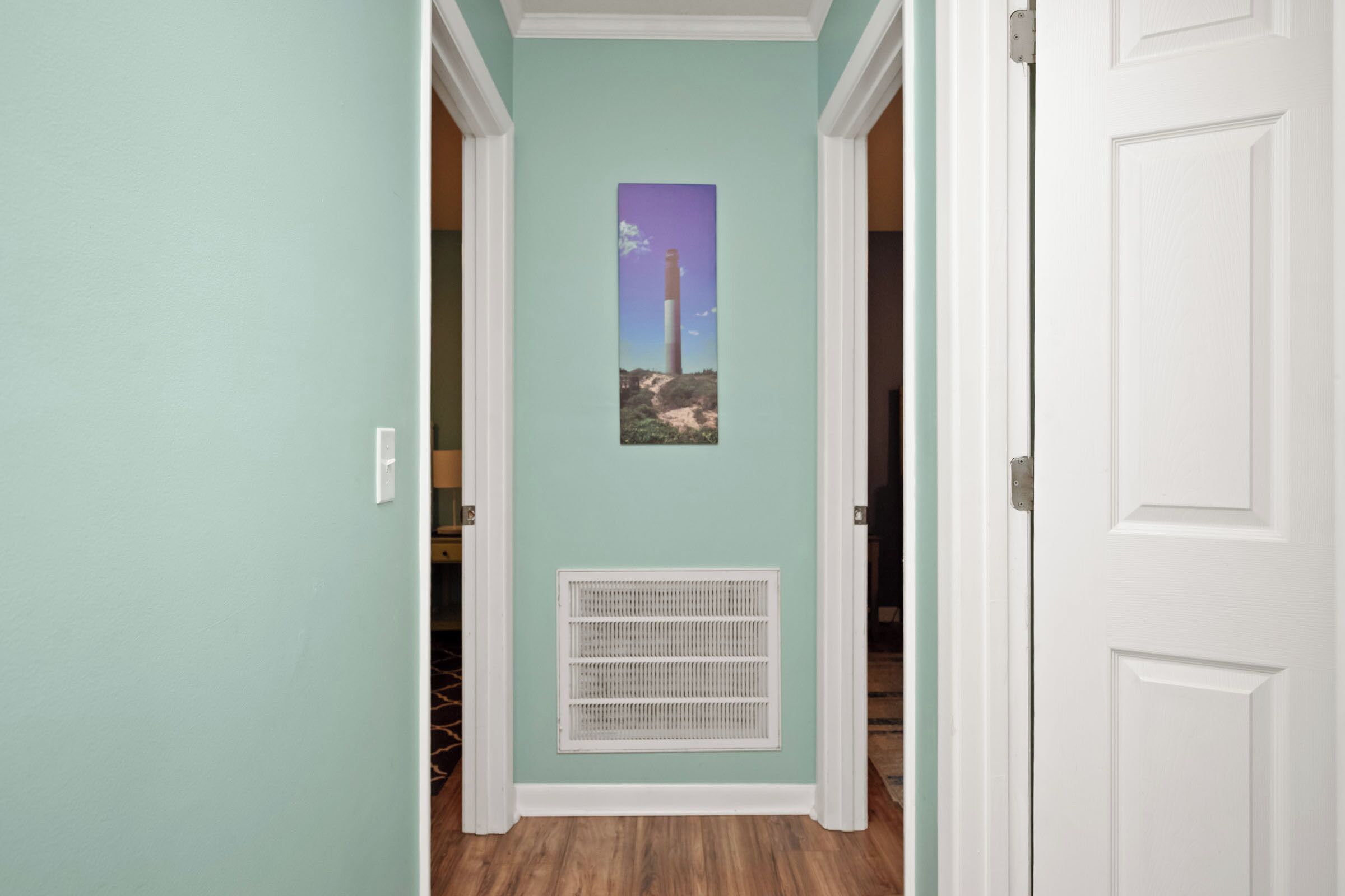 A hallway with a light green wall, a vent, and a door.