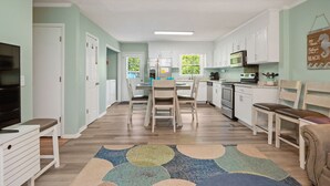 Een ruime keuken met witte kasten, een eettafel met stoelen en een groot raam dat voor natuurlijk licht zorgt.