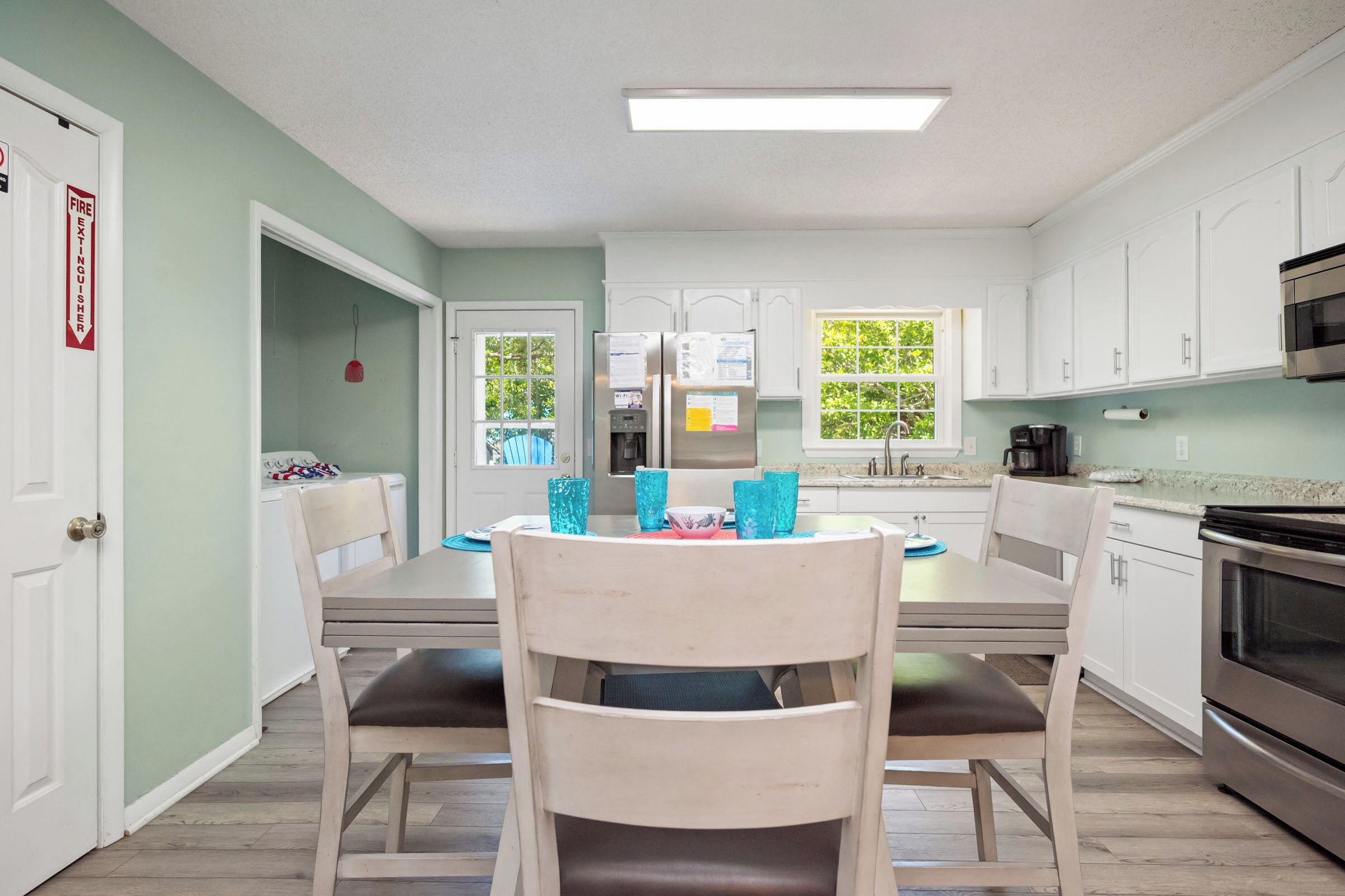 A modern kitchen with white cabinets, a stainless steel oven, and a dining area with two chairs and a table.