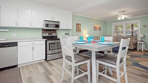 Een moderne keuken met witte kasten, een magnetron en een vaatwasser. Er is een eettafel met stoelen en een plafondventilator erboven.