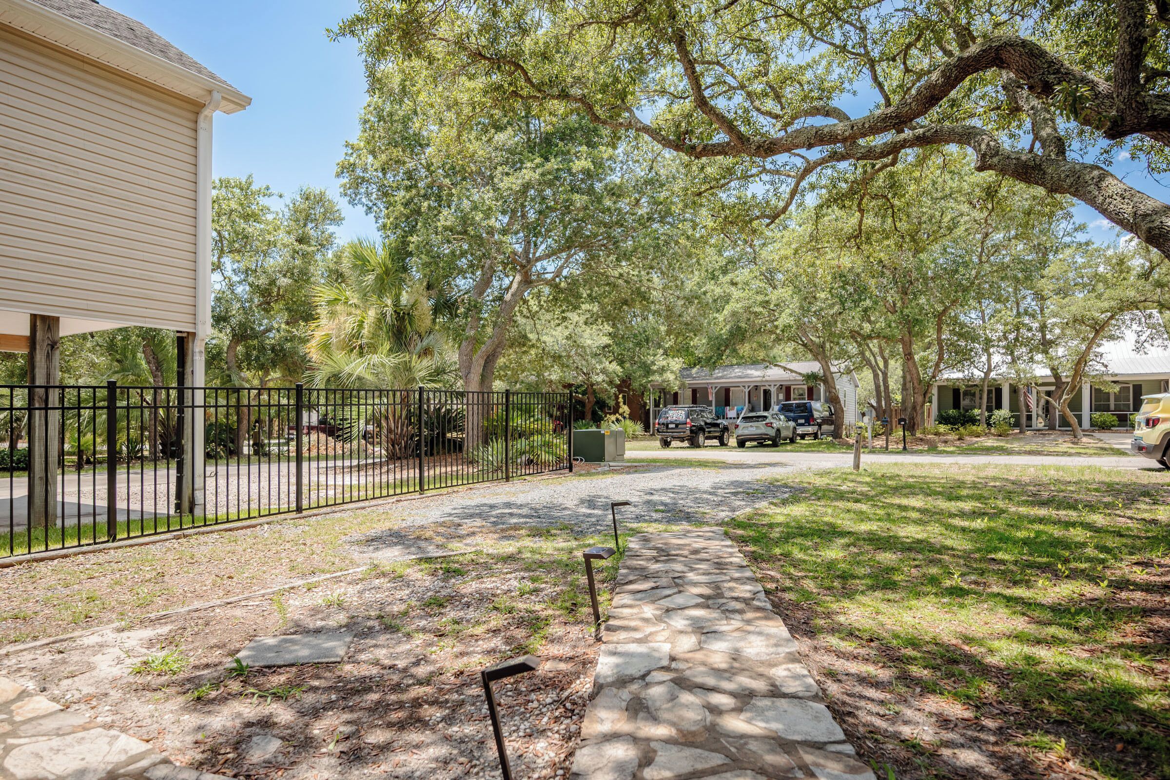 A residential area with a paved pathway, a stone wall, and a black metal fence.