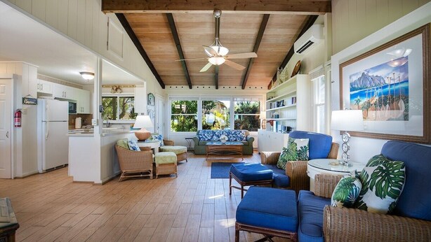 A spacious living area with a ceiling fan, a sofa set, and a dining area with a kitchen in the background.