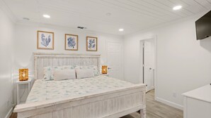 Een slaapkamer met een houten bed, witte muren en kunstwerken in lijsten erboven.