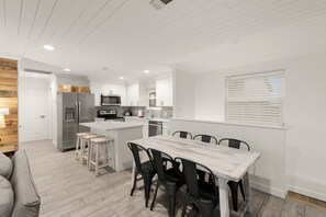 A modern kitchen with white cabinetry, a central island with stools, a dining table with chairs, and a built-in oven. - 200 feet from Beach Access, Ocean views, and Pet Friendly (Panama City Beach)