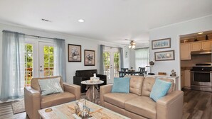 A spacious living room with a beige sofa, a coffee table, and a dining area with a table and chairs. - Pelican Park: Dog-friendly Home Overlooking Canal with Backyard Fireplace, Just (Oak Island)