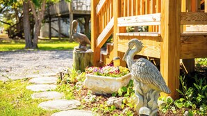 A wooden deck with a stone pathway, a bird statue, and a planter with flowers. - Pelican Park: Dog-friendly Home Overlooking Canal with Backyard Fireplace, Just (Oak Island)