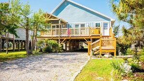 A two-story building with a covered porch and a flag. - Pelican Park: Dog-friendly Home Overlooking Canal with Backyard Fireplace, Just (Oak Island)