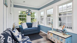 A room with a blue sofa, a patterned couch, a wooden cabinet, and a decorative bird sculpture. - Pelican Park: Dog-friendly Home Overlooking Canal with Backyard Fireplace, Just (Oak Island)