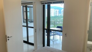 Ein Schlafzimmer mit Bett, einer Schiebetür, die auf einen Balkon führt, und einem Fenster mit Blick auf die Stadt.