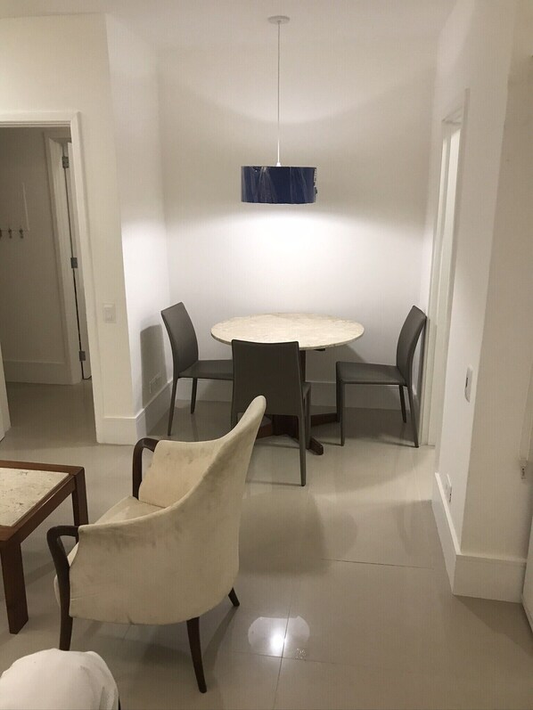 Un comedor con una mesa redonda y seis sillas, una lámpara colgante y una puerta que da a otra habitación.