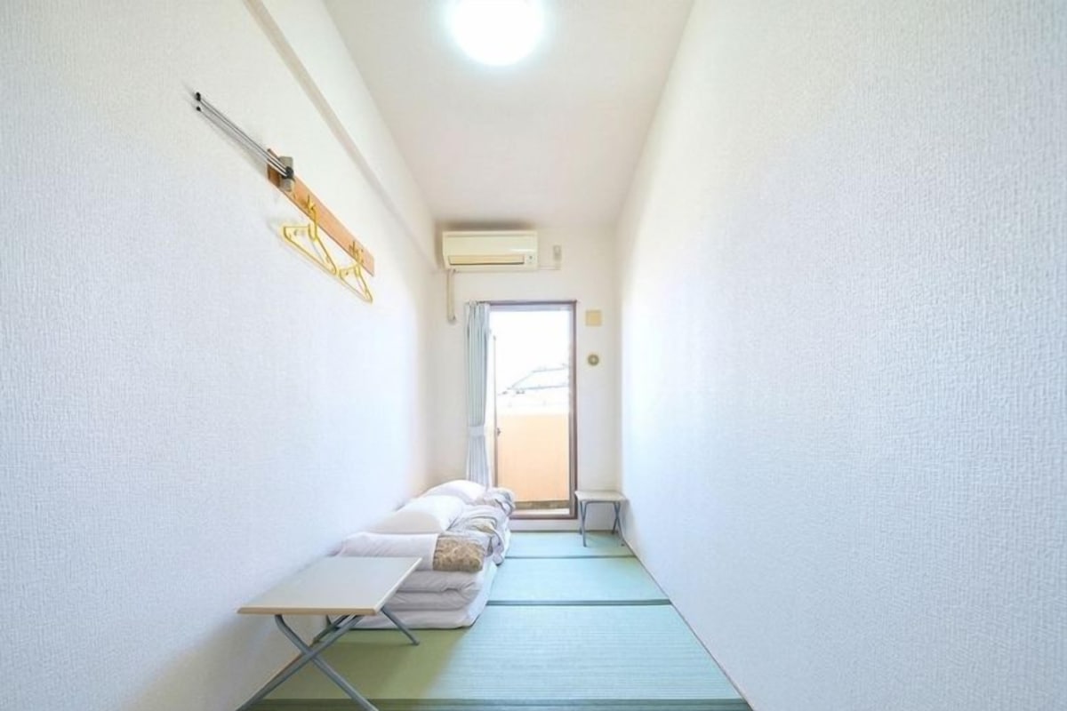 A narrow hallway with a bed, a small table, and a wall-mounted heater.