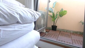 Uma cama com roupa branca, um vaso com planta e um deck de madeira.