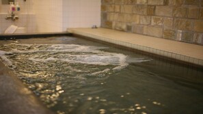 A spa pool with water jets, a tiled wall, and a stone wall in the background. - Hotel Accela (Tokyo)