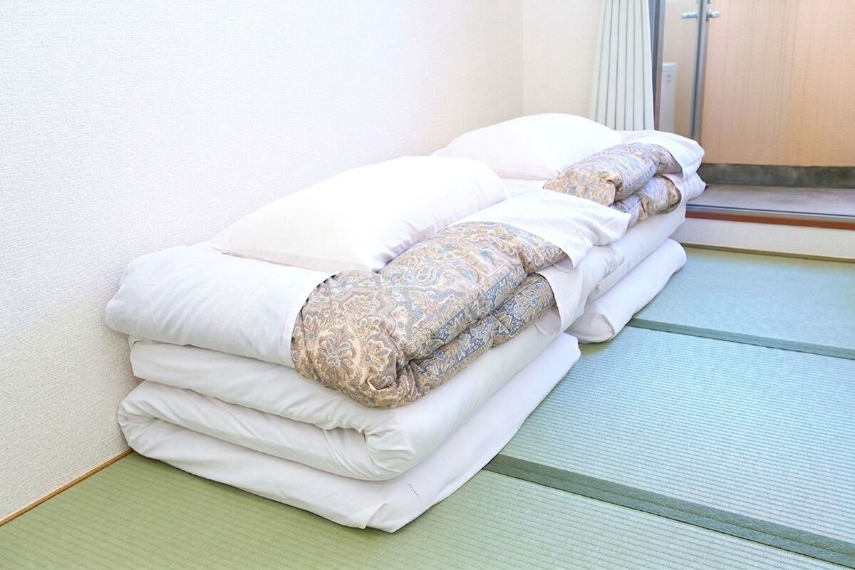 A neatly made bed with white and patterned bedding in a room with a green floor and a white wall.