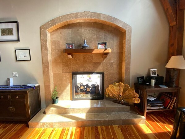 Una chimenea con arco de piedra, cuadros enmarcados en la repisa, y una planta pequeña a un lado.