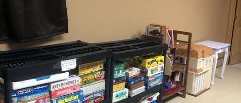 A room with a black shelf filled with board games, a black curtain, a wall-mounted air conditioner, and a small table with a basket.