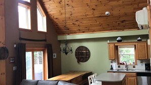 A spacious living area with a gray sectional sofa, a wooden ceiling fan, and a view of the kitchen with wooden cabinets and a stainless steel refrigerator. - Windham Mountain Chalet with Treehouse sleeps 15, Game Room & fireplace (Windham)