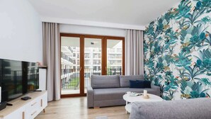 A modern living room with a grey sofa, a flat-screen TV on a wooden console, and a balcony with a view of residential buildings. - Spacious Apartment for 7 Persons | Parking | Close to the Station (Kraków)