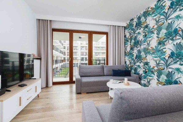 Relax in this stylish living room with a large flat-screen TV, comfortable sofa, and sliding glass door leading to a balcony with a view.