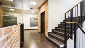 A modern interior with a brick wall, a staircase with black railings, and a tiled floor. - Spacious Apartment for 7 Persons | Parking | Close to the Station (Kraków)