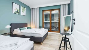 A modern hotel room with a bed, bedside tables, a mirror, and a view of the outside through a glass door. - Spacious Apartment for 7 Persons | Parking | Close to the Station (Kraków)