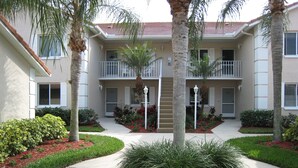 A residential building with a central courtyard, surrounded by palm trees and well-maintained landscaping. - Just Listed for 2027 Season:  Glen Eagle Golf & Country Club (Naples)