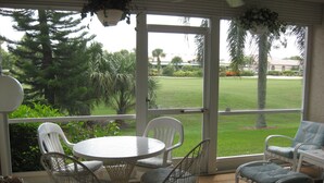A covered patio with a round table and chairs, overlooking a well-maintained lawn and trees. - Just Listed for 2027 Season:  Glen Eagle Golf & Country Club (Naples)