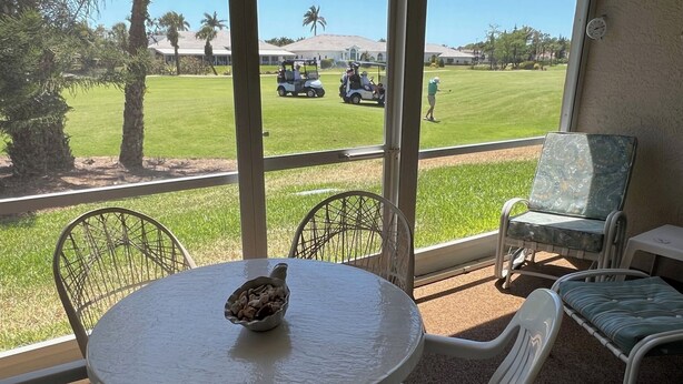 A patio with a round table and chairs, overlooking a golf course with a golf cart and a golfer. - Just Listed for 2027 Season:  Glen Eagle Golf & Country Club (Naples)