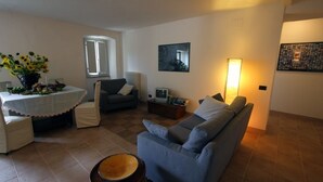 Ein Wohnzimmer mit einem blauen Sofa, einem Tisch mit Blumen in einer Vase, einer Lampe und einem gerahmten Bild an der Wand.