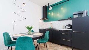 A modern kitchen with teal walls, black cabinets, and a herringbone wood floor. There is a dining table with teal chairs and a vase of flowers.