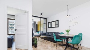 A modern living room with a herringbone floor, a sofa, a dining table with chairs, and a pendant light.