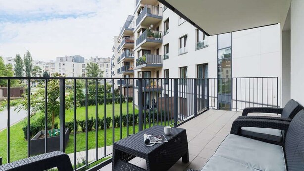Un balcón con sofá, una mesita y vista a un edificio residencial.