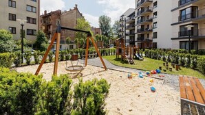 Un parque infantil con columpios y toboganes, rodeado de arbustos bien cuidados y una zona de arena.