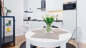 Una cocina moderna con armarios blancos, horno integrado y una mesa de comedor redonda con un florero.